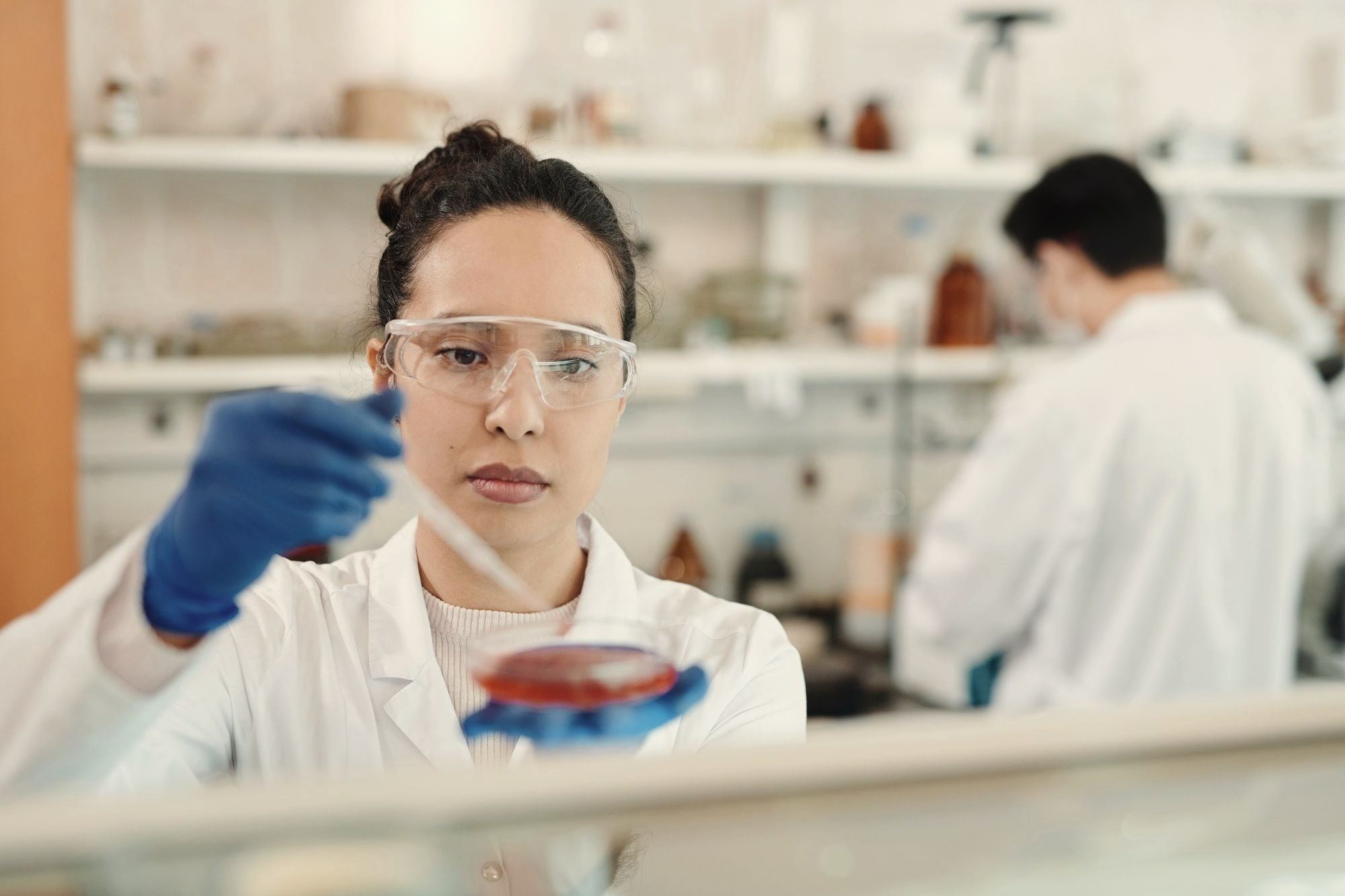 A student in safety glasses and a lab coat working with a sample at the bench