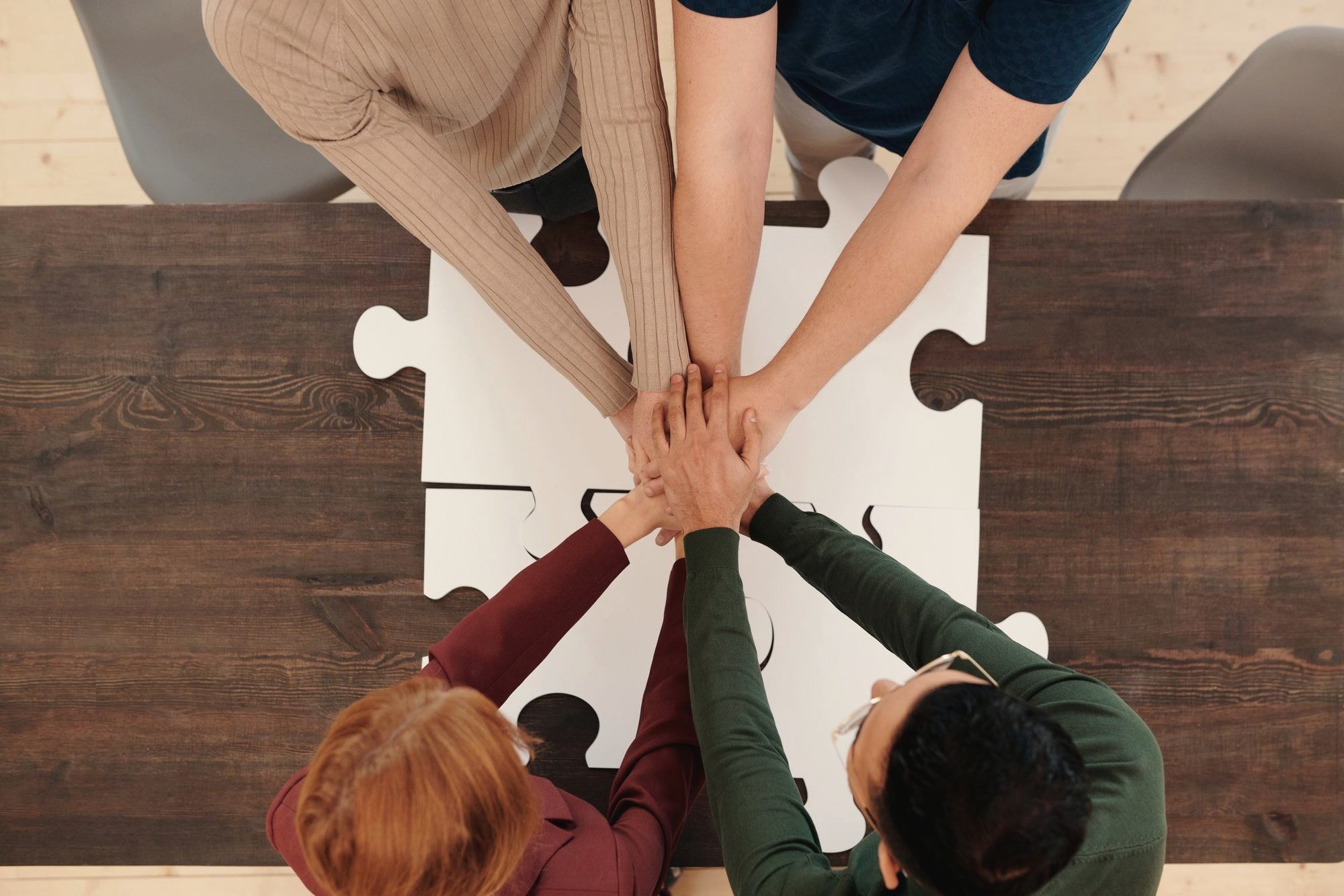 Several hands meeting in the middle of a table over large puzzle pieces