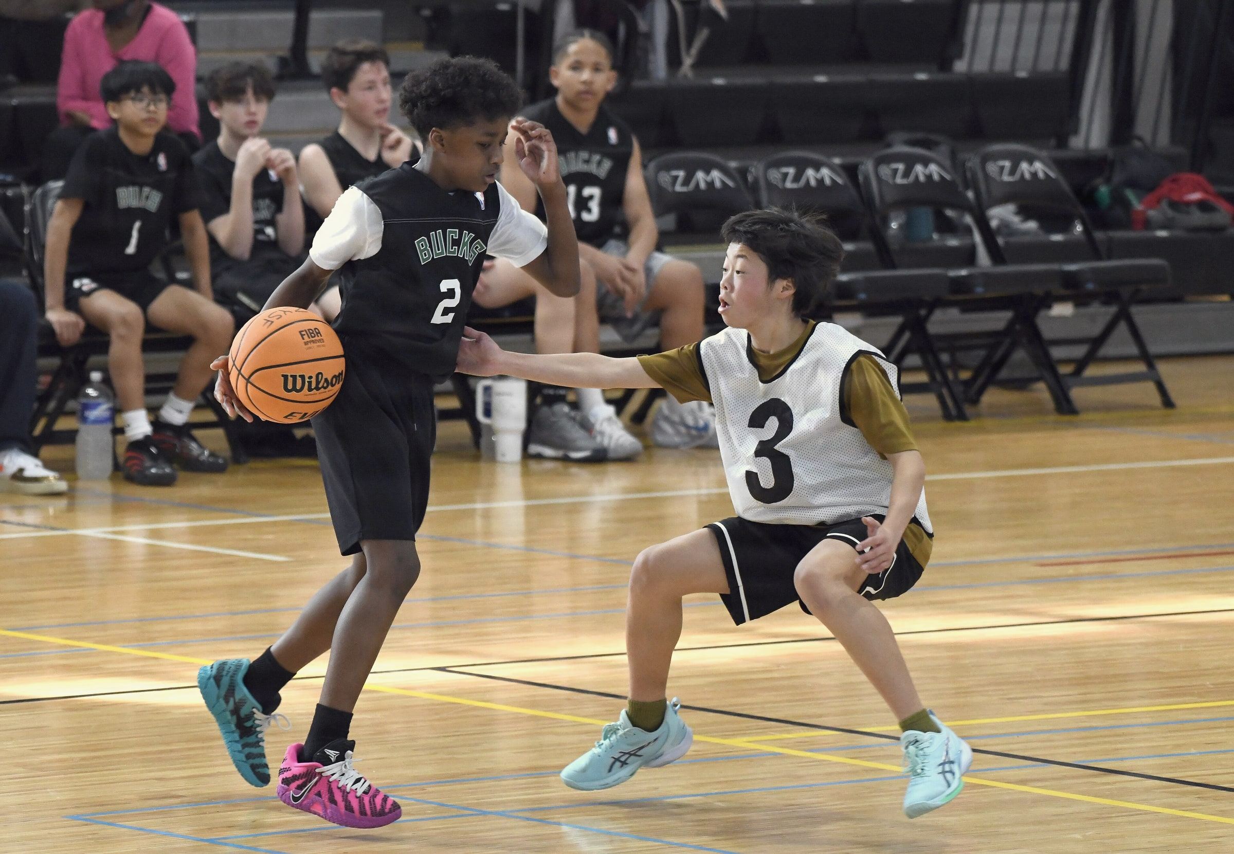 Two teenagers in a youth basketball game, one driving past a defender